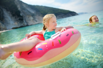 Cute young sisters floating on toy ring at Myrtos beach, the most famous and beautiful beach of Kefalonia, a large coast with turqoise water and white coarse sand.