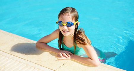 Cute young girl wearing swimming goggles having fun in outdoor pool. Child learning to swim. Kid having fun with water toys.