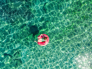 Aerial top down view of cute young girl floating on toy ring at Emplisi Beach, picturesque stony beach in a secluded bay, with clear waters popular for snorkelling.