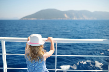 Adorable young girl enjoying ferry ride staring at the deep blue sea. Child having fun on summer family vacation in Greece.