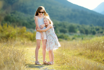Two cute young sisters laughing and hugging on warm and sunny summer day during family vacations in Greece