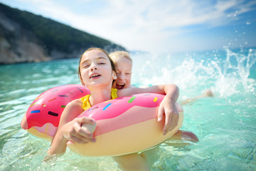Cute young sisters floating on toy ring at Myrtos beach, the most famous and beautiful beach of Kefalonia, a large coast with turqoise water and white coarse sand.