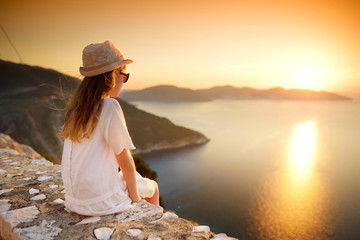 Cute young girl enjoying the view of picturesque jagged coastline of Kefalonia on summer sunset.
