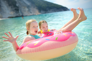Cute young sisters floating on toy ring at Myrtos beach, the most famous and beautiful beach of Kefalonia, a large coast with turqoise water and white coarse sand.
