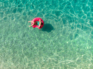 Aerial top down view of cute young girl floating on toy ring at Myrtos beach, the most beautiful beach of Kefalonia, a large coast with turqoise water and white coarse sand.