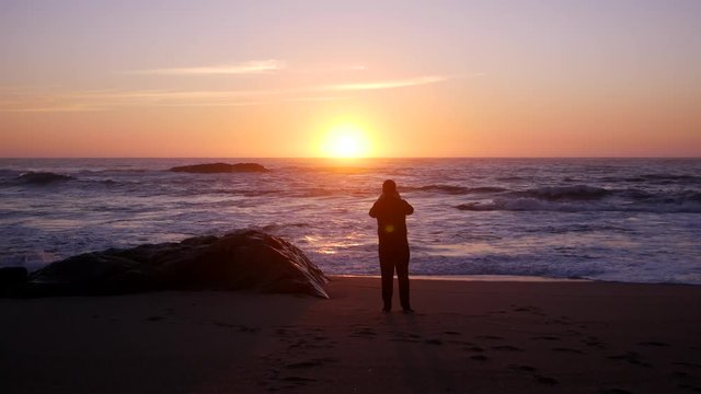 Man in silhouette at sunset on beach, taking photo with mobile phone