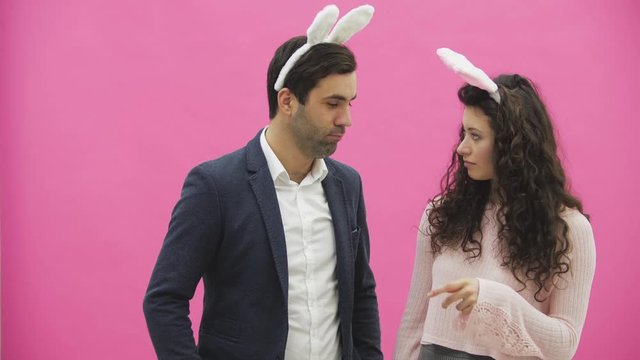 Young lovers couple on the pink background. With hackneyed ears on the head. During this, the photos of Sephi on the phone are very sincere smiles. Funny people.