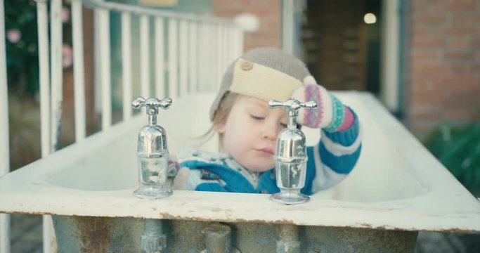 Little toddler with a hat playing in old bathtub outdoors