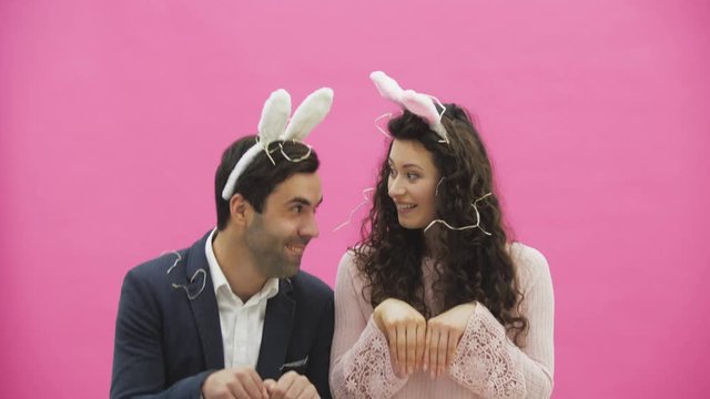 Young sexy couple on pink background. With hackneyed ears on the head. During this reproduction sexual rabbit movements and looks, after a while go out of the frame.