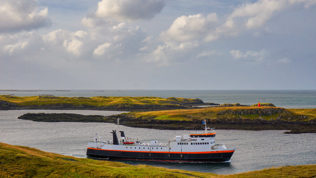 Ferry leaving from Port Baldur in Stykkisholmur and head to   in northern fjord of Iceland with cloudy sky above.