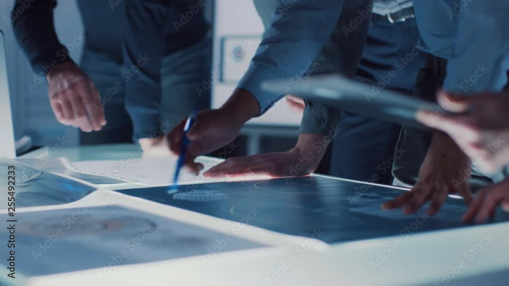 Poster engineer, scientists and developers gathered around illuminated conference table in technology resea