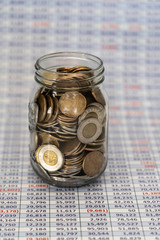Jar full of coins with Spreadsheet in bavckground