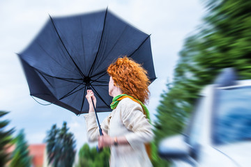 a woman with red hair tries to hold her umbrella in a storm