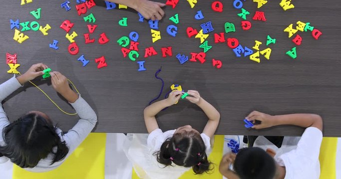 Asian teacher lets Asian student string alphabet toy together, concept for English class.