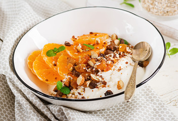 Bowl of homemade granola with yogurt and tangerine on white wooden table. Fitness food.