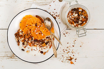 Bowl of homemade granola with yogurt and tangerine on white wooden table. Fitness food. Top view