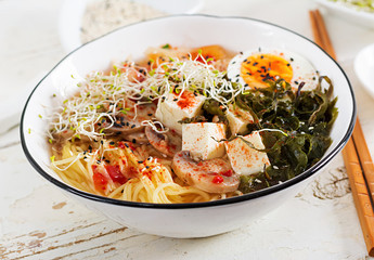 Miso Ramen Asian noodles with cabbage kimchi, seaweed, egg, mushrooms and cheese tofu in bowl on white wooden table. Korean cuisine.