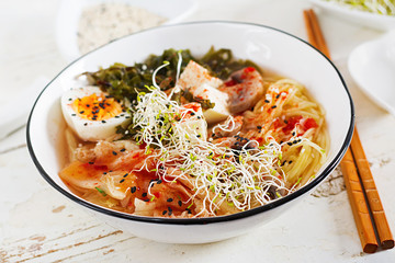 Miso Ramen Asian noodles with cabbage kimchi, seaweed, egg, mushrooms and cheese tofu in bowl on white wooden table. Korean cuisine.