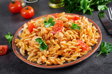 Pasta Fusilli  with tomatoes, chicken meat and parsley on plate on dark table.