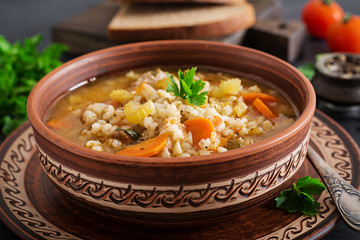 Barley soup with carrots, tomato, celery and meat on a dark background.
