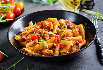 Penne pasta in tomato sauce with meat, tomatoes decorated with pea sprouts on a dark table.