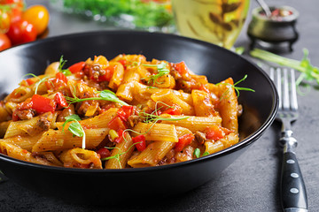 Penne pasta in tomato sauce with meat, tomatoes decorated with pea sprouts on a dark table.