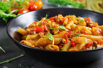 Penne pasta in tomato sauce with meat, tomatoes decorated with pea sprouts on a dark table.