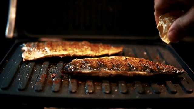 Chef Pouring Grilled Fish With Lemon juice.Pouring Lemon Juice Over The Top Of Mackerel Steak While Frying It On Grill Barbecue In Slow Motion.Close-up Shot Chef Pouring Grilled Sardines With Lemon 