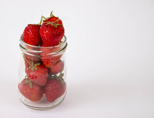 Strawberrys many with both ripe fruit and  not fruit ripe in jar glass and strawberrys all laid are on a white background.