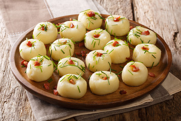 Boiled potato dumplings with fried bacon and fresh green onions close-up on a plate. horizontal