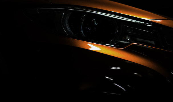 Closeup headlight of shiny orange luxury SUV compact car. Elegant electric car technology and business concept. Hybrid auto and automotive. Car parked in showroom or motor show. Car dealership.
