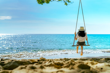 Asian woman in casual style wear hat swing the swings at sand beach  and looking beautiful tropical...