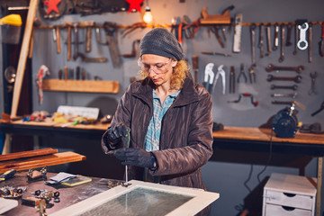 Woman carpenter sanding old window in a retro workshop.