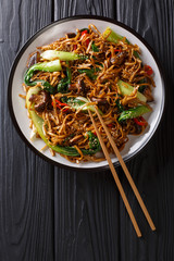 Asian vegetarian food udon noodles with baby bok choy, shiitake mushrooms, sesame and pepper close-up on a plate. Vertical top view © FomaA