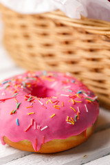 Concept of cooking, baking and food - close-up. Donut in pink icing with colored sprinkling on the background of a wicker basket. Trend colors.