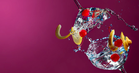 Cocktails in glasses with splashes garnished with lemon and cherries.