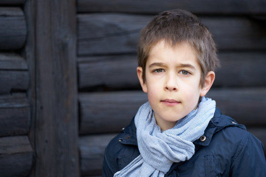 Portrait of a boy with blue scaf in front of a dark wooden background looking in camera