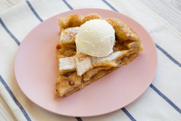 Slice of home-baked apple pie with ice cream on pink plate, side view. Closeup.