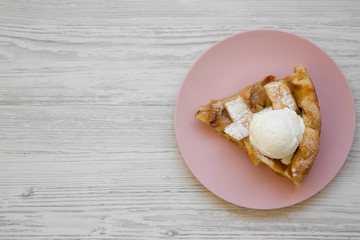 Slice of homemade apple pie with ice cream on pink plate on white wooden table, top view. Flat lay, overhead, from above. Copy space.