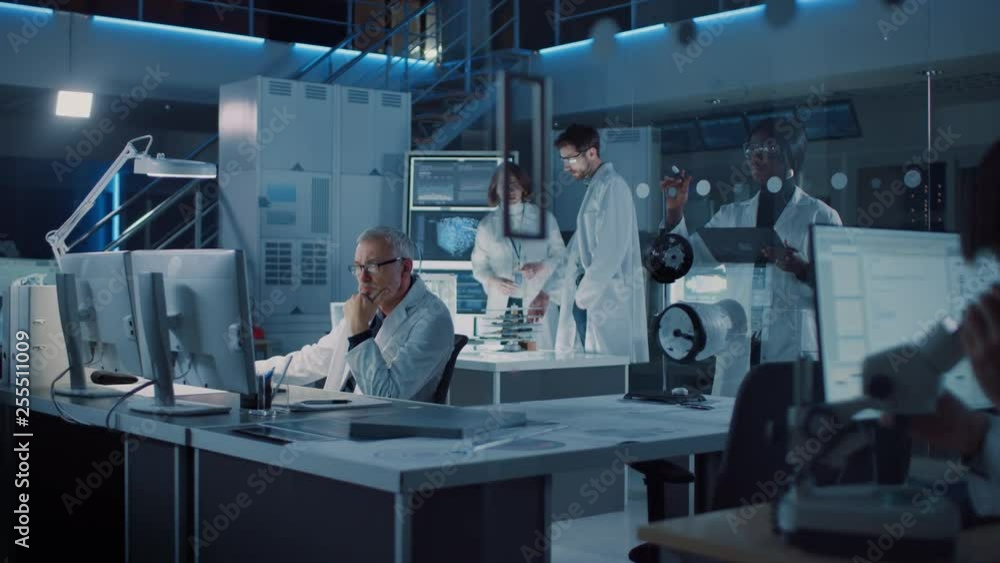 Poster Diverse International Team of Industrial Scientists and Engineers Wearing White Coats Working on Heavy Machinery Design in Research Laboratory. Professionals Using Computers and Talking