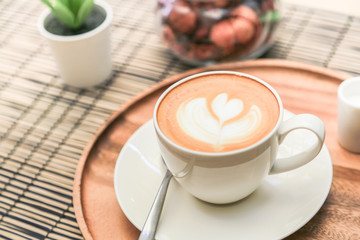 Hot latte coffee on a wooden tray with warm light