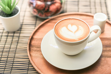 Hot latte coffee on a wooden tray with warm light