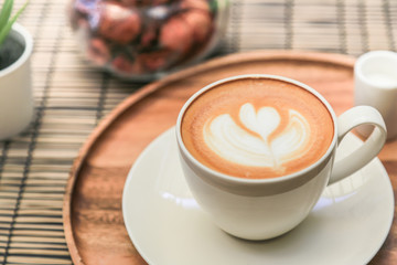 Hot latte coffee on a wooden tray with warm light