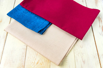 close up of cloth napkins of beige, blue and burgundy colors on rustic white wooden table. Shallow depth of field.