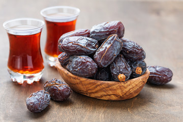 Fresh Medjool Dates in a bowl with tea on wooden background.