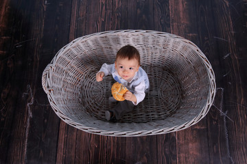 A tiny child eats a dry bun in a basket woven from a wicker tree.