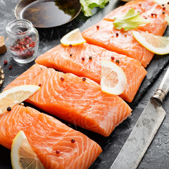 Raw salmon fillet and ingredients for cooking on a dark background.