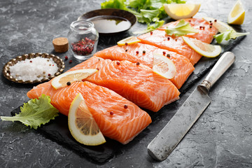 Raw salmon fillet and ingredients for cooking on a dark background.