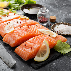 Raw salmon fillet and ingredients for cooking on a dark background.