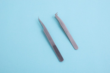 two tweezers for eyelash extensions on a turquoise background